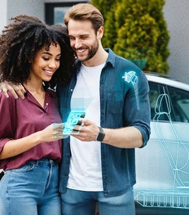 A couple stood infront of a EV car that is charging looking at a device